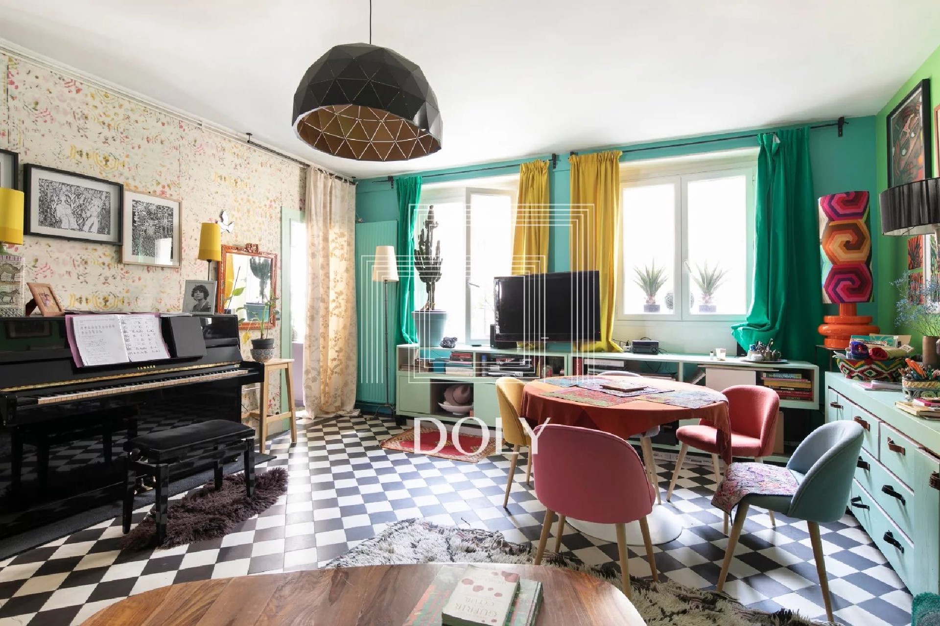 Appartement 3 pièces de 86 m² - L'espace de vie, avec coin repas, TV et piano, est visible. La pièce est entièrement décorée dans des tons vifs. De grandes baies vitrées laissent entrer la lumière naturelle.