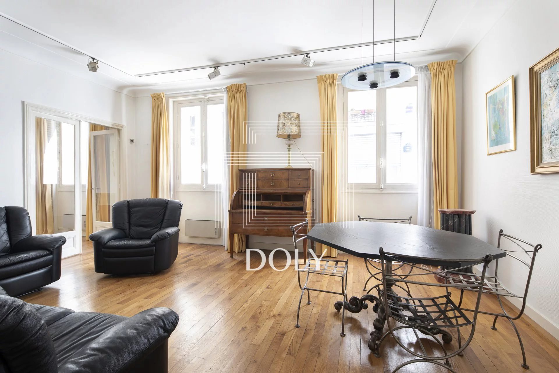 Appartement 3 pièces de 77 m², Parc de Montsouris : l'espace de vie est doté d'un magnifique parquet, d'un canapé et d'un coin repas. Deux grandes baies vitrées laissent entrer la lumière.